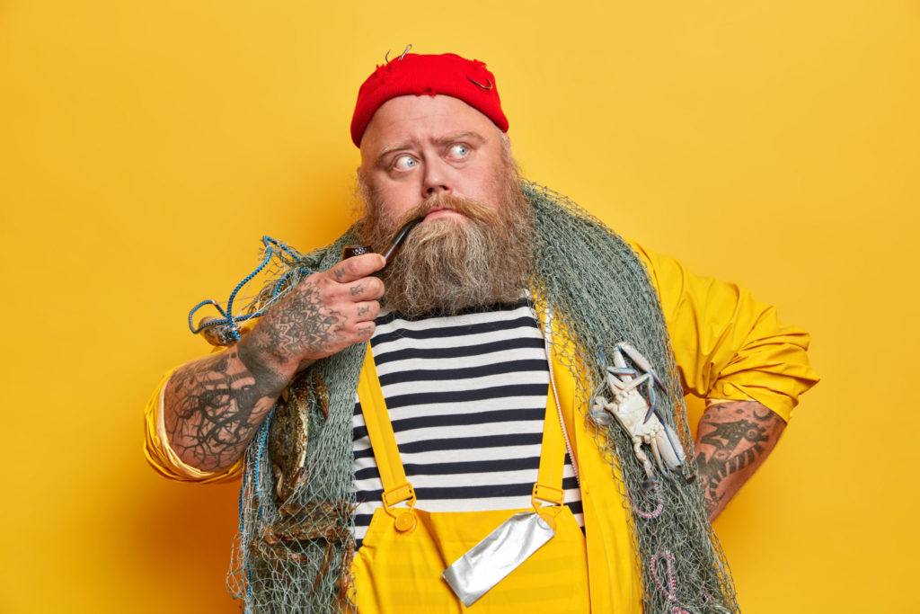 old-experienced-bearded-sailor-thinks-about-day-sea-poses-with-fishing-gear-smokes-pipe-dressed-overalls-red-hat.